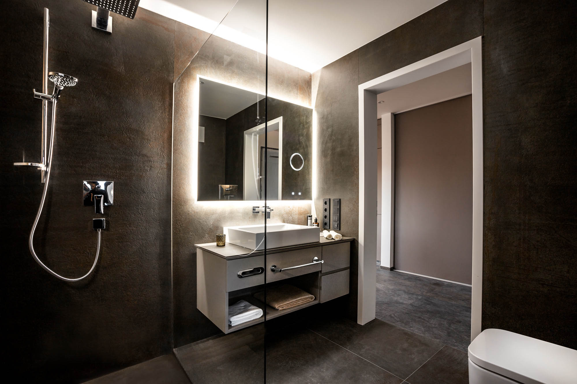 Das moderne Bad mit separater Dusche ist dunklem Steinboden ausgestattet. auch die Wände sind in dunkel gehalten.